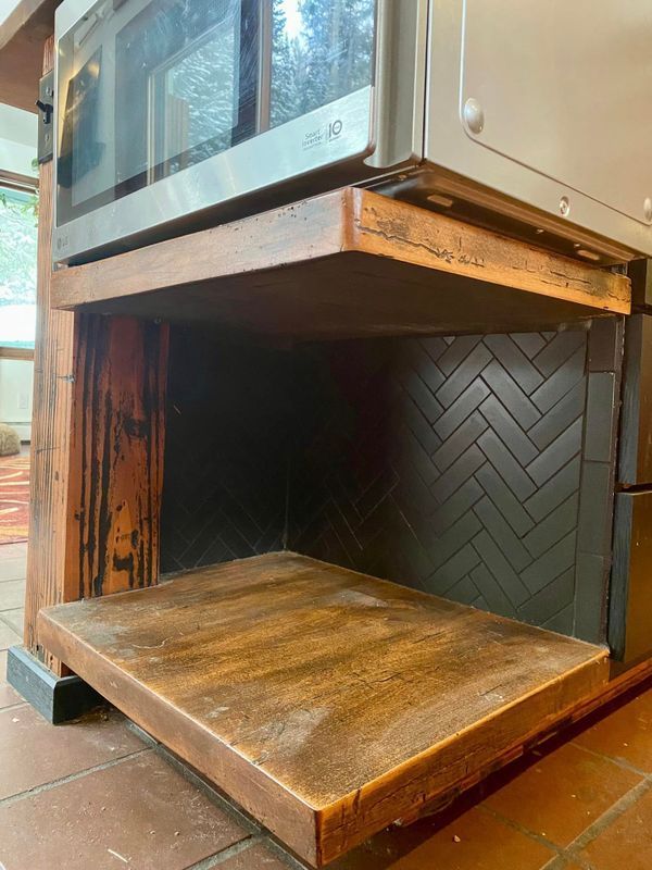 Open wooden cabinet or niche with a hinged lower shelf and dark herringbone back panel