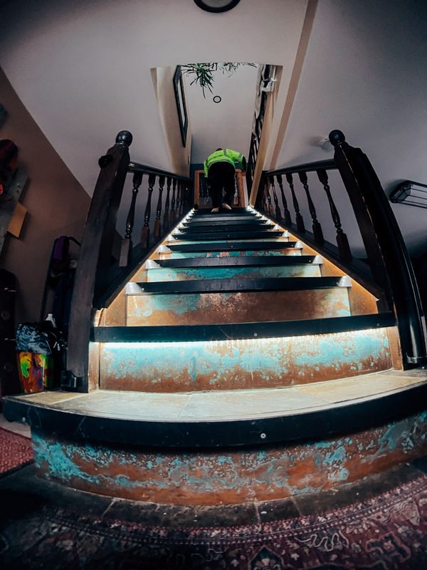 Curved staircase with glowing teal-lit steps and black railings in a dim interior, viewed from below