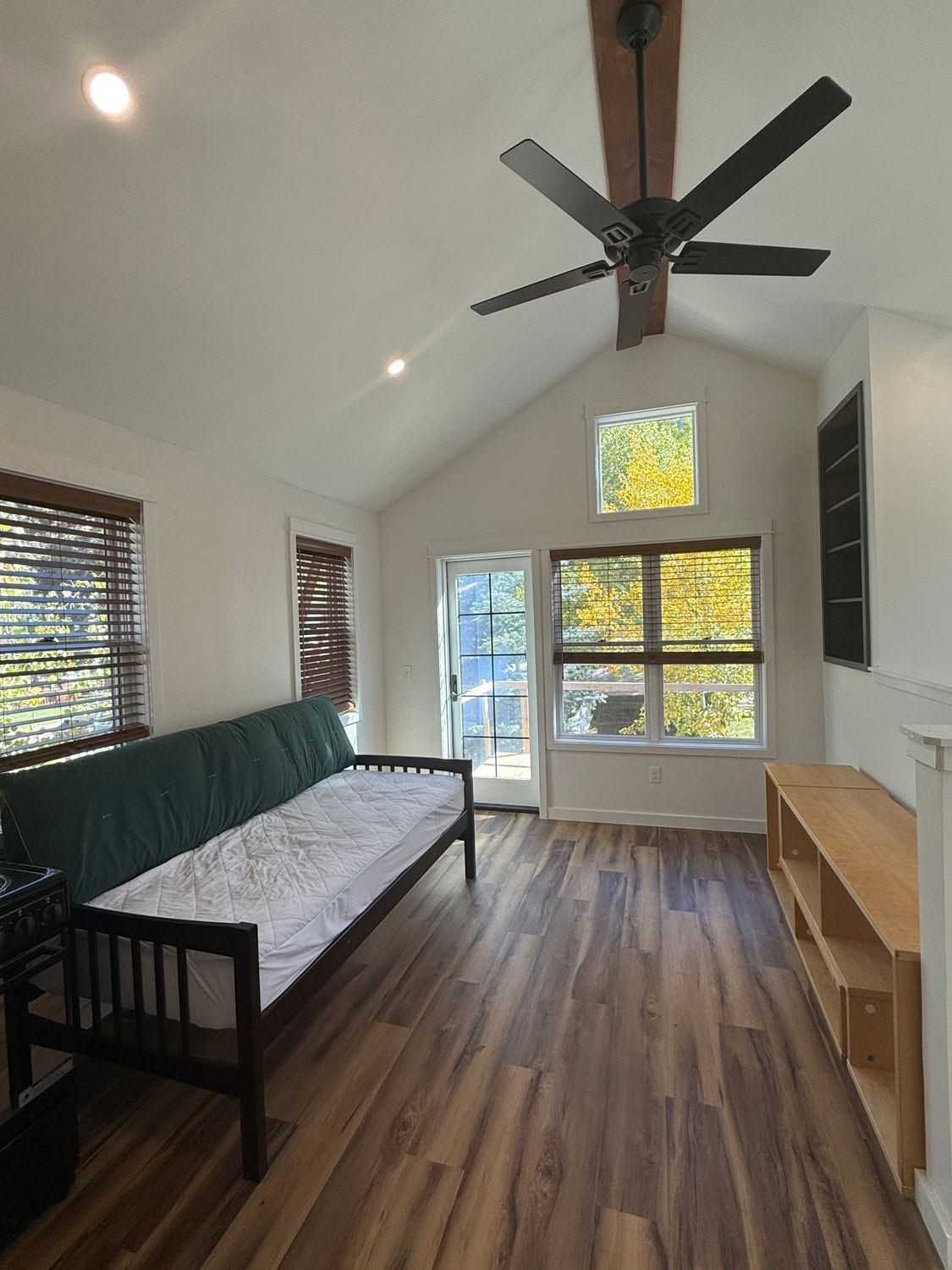 Bright sunroom with green daybed, wood floors, ceiling fan, and large windows overlooking outdoors