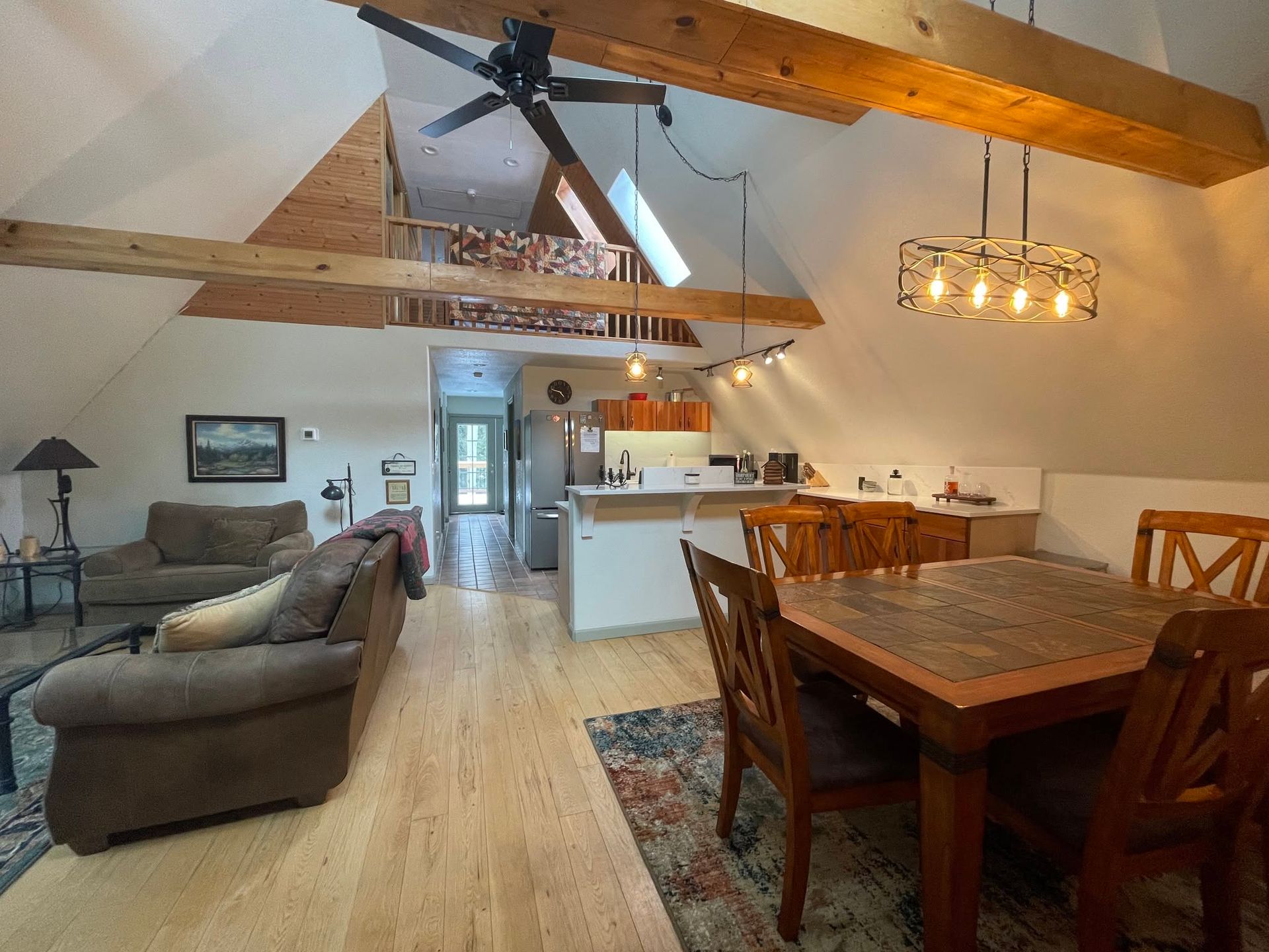 Open loft living-dining room with exposed beams, sofa, wooden table, and kitchen in the background