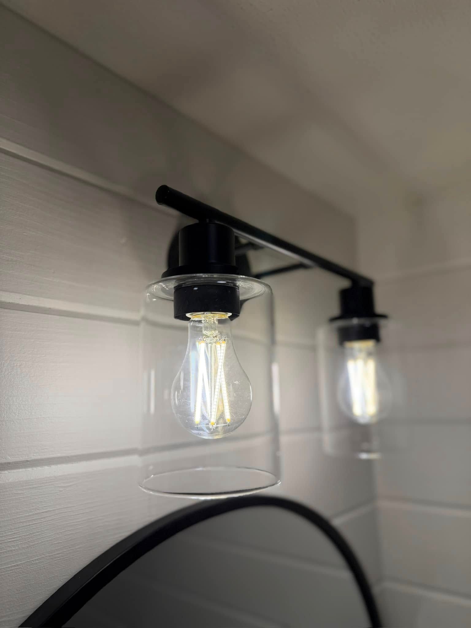 Two wall-mounted clear glass light fixtures with exposed bulbs on a white shiplap wall