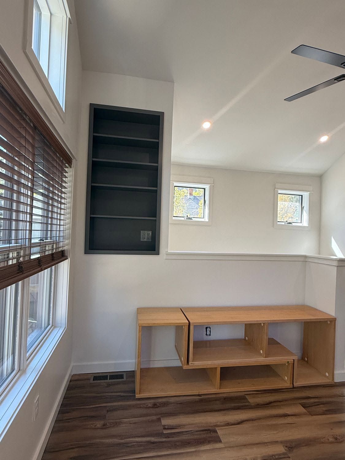 Bright empty room with wood floors, built-in shelves, windows, and a wooden desk against the wall