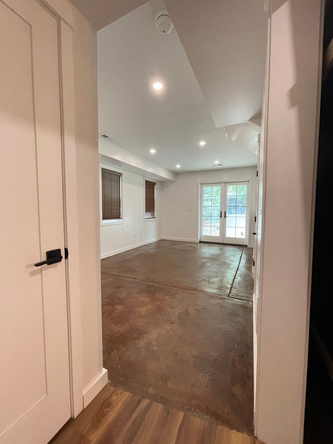 Empty bright room with white walls, recessed lights, wood floor, and French doors to a patio.