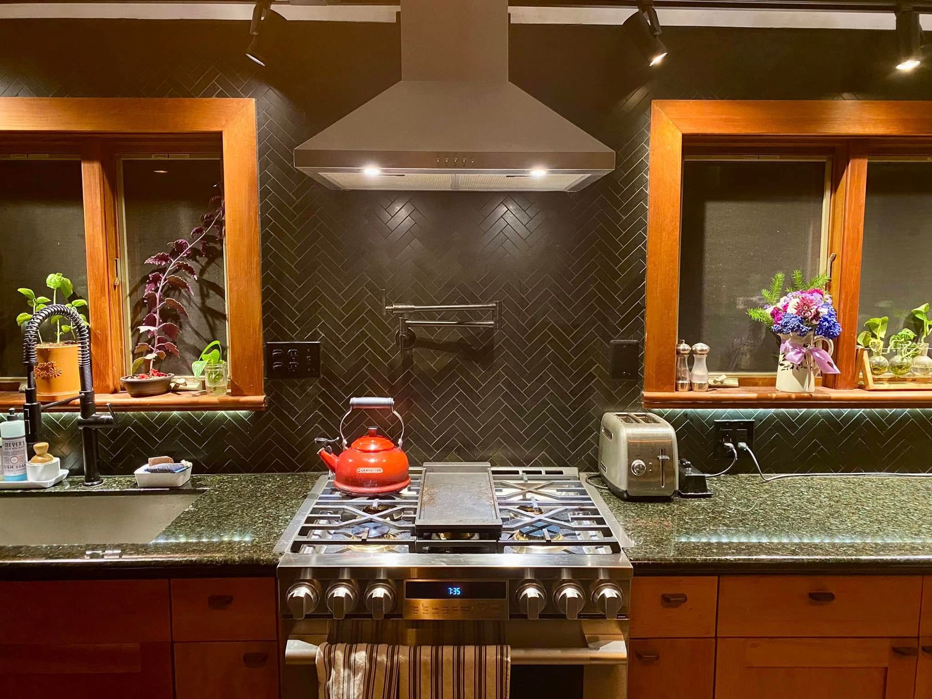 Modern kitchen with stainless steel stove, red kettle, dark backsplash, and granite countertops.