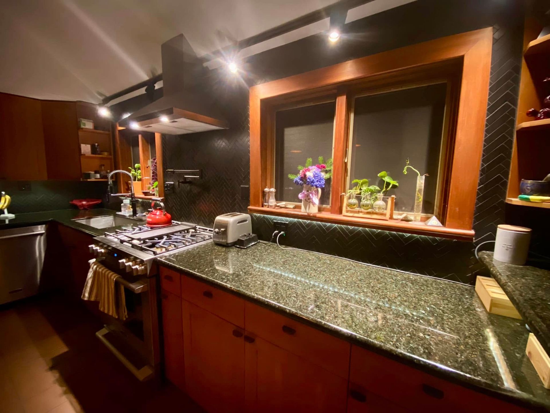Warm kitchen with dark cabinets, granite counters, and a window above the sink with flowers.