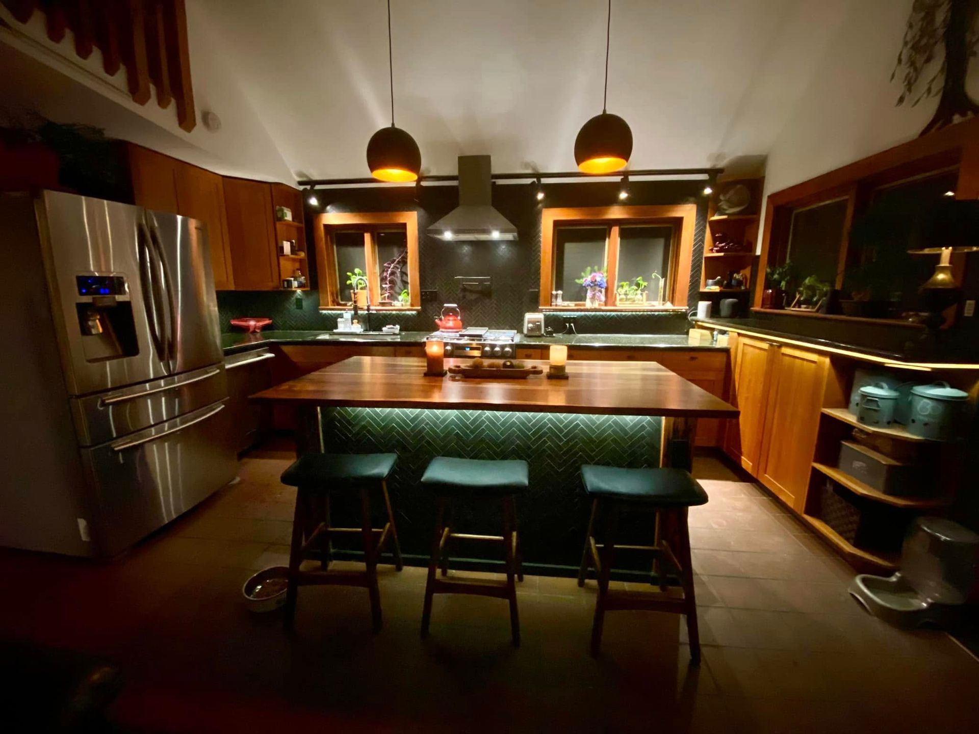 Warm, modern kitchen with stainless steel fridge, island seating, and amber pendant lights