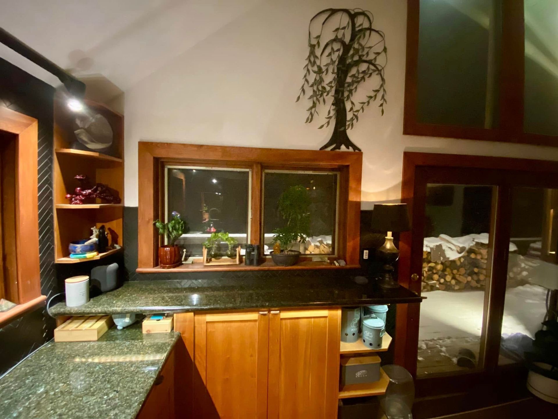 Kitchen counter and sink with wood cabinets, granite countertops, and a window at night.