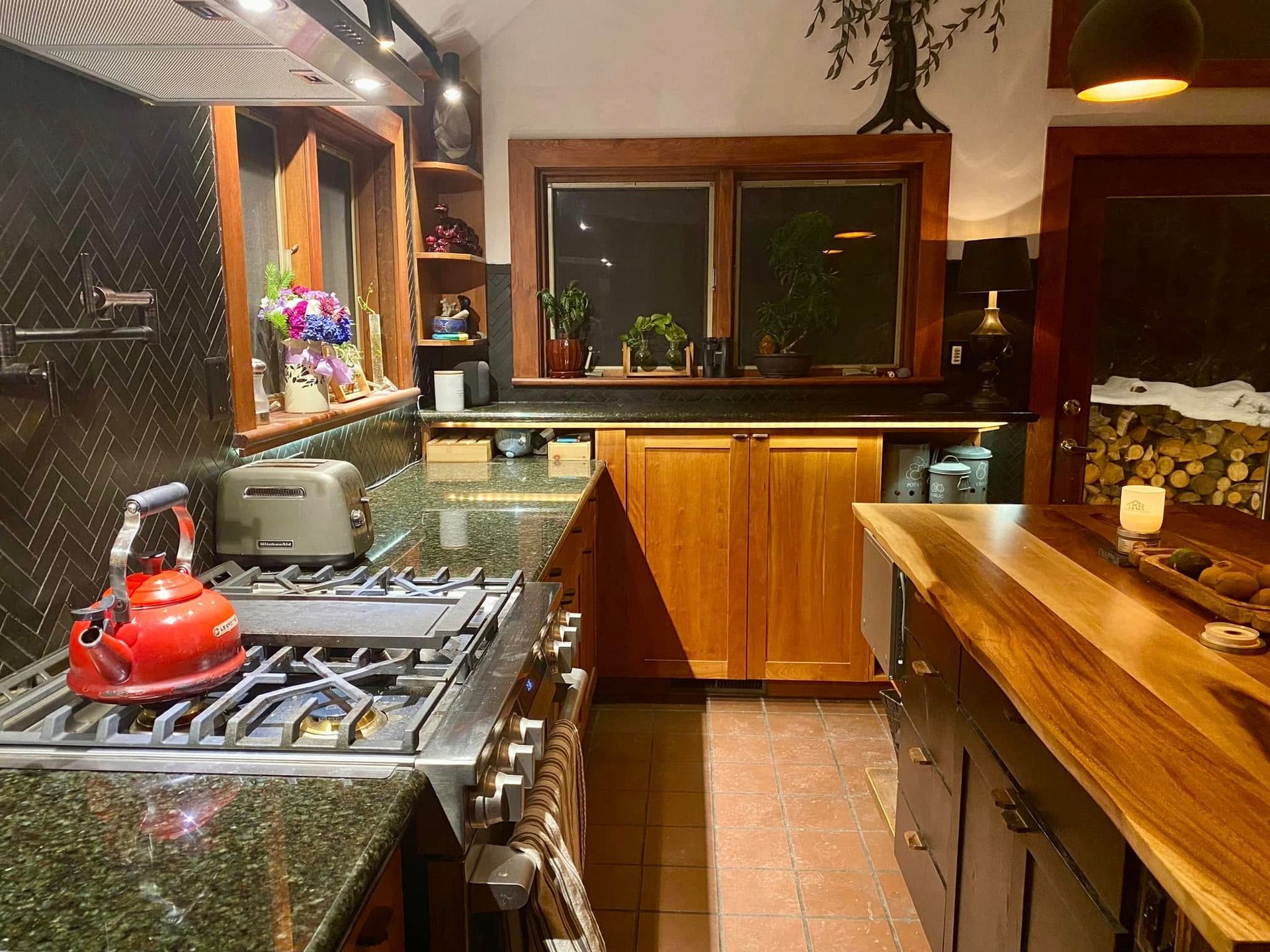 Modern kitchen with wooden cabinets, black countertops, gas stove, red kettle, and a window over the sink.