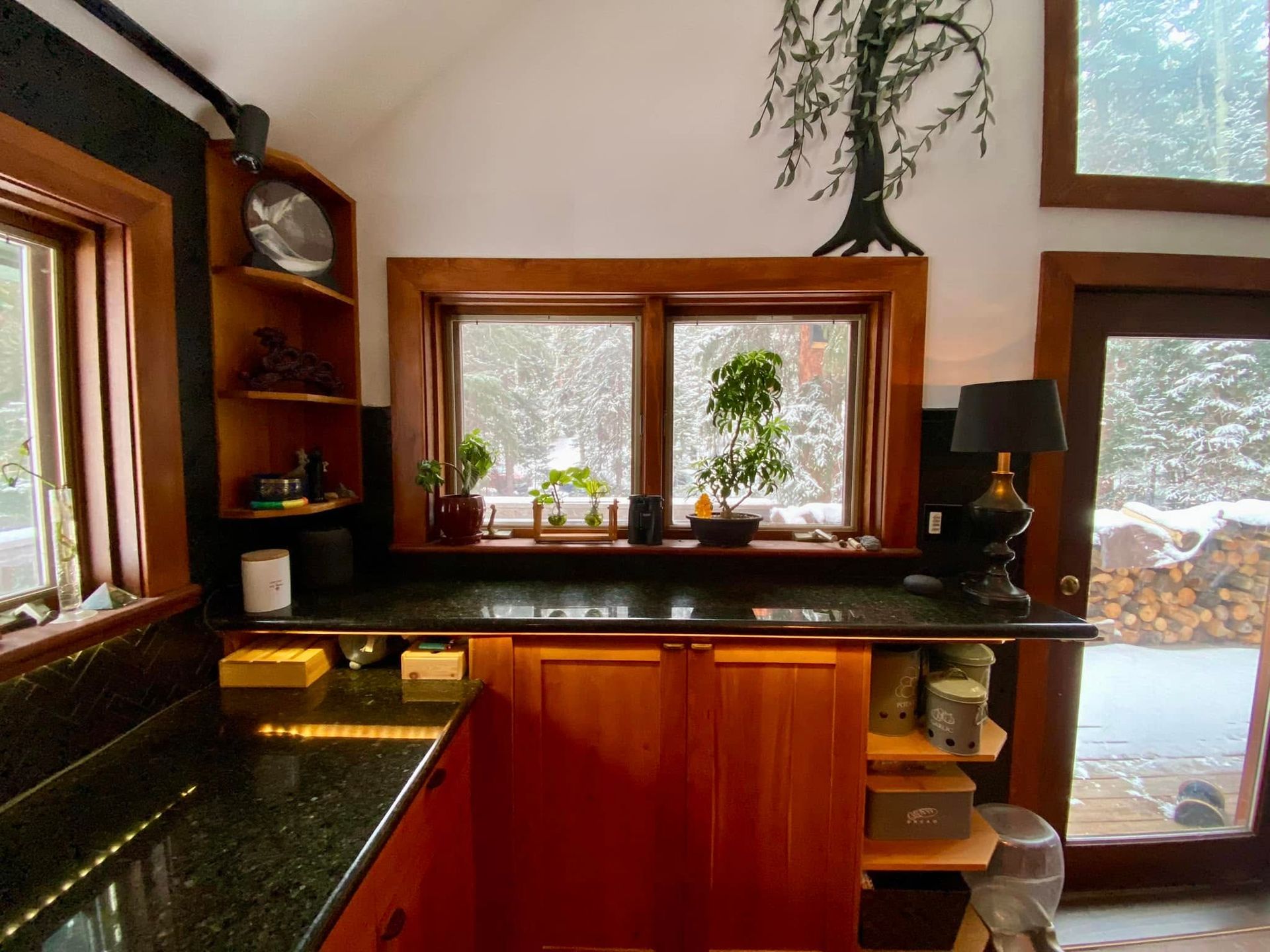 Compact kitchen with wood cabinets, dark counters, and large windows overlooking snow outside.