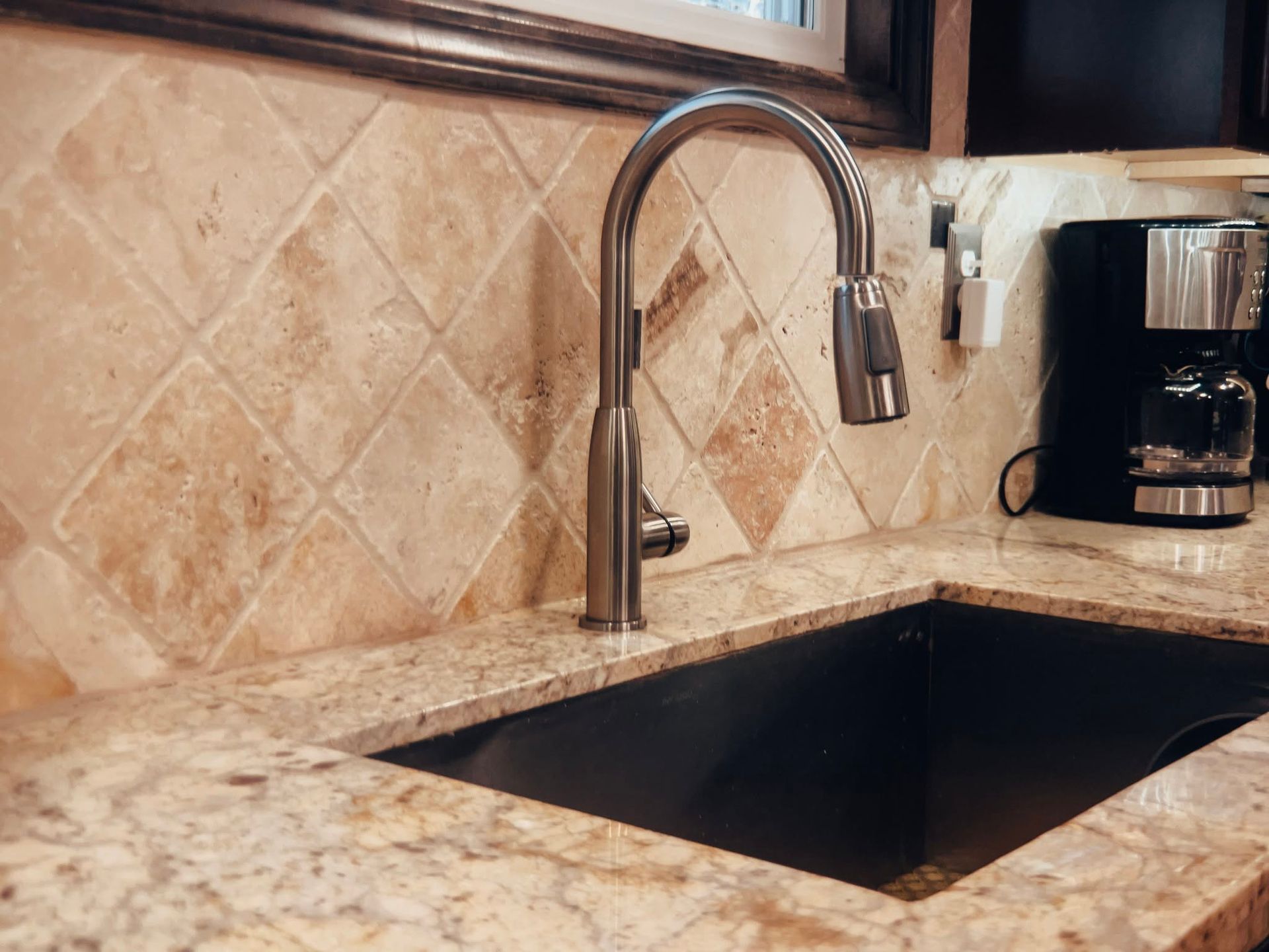 Kitchen sink with chrome faucet, beige tile backsplash, and coffee maker on countertop