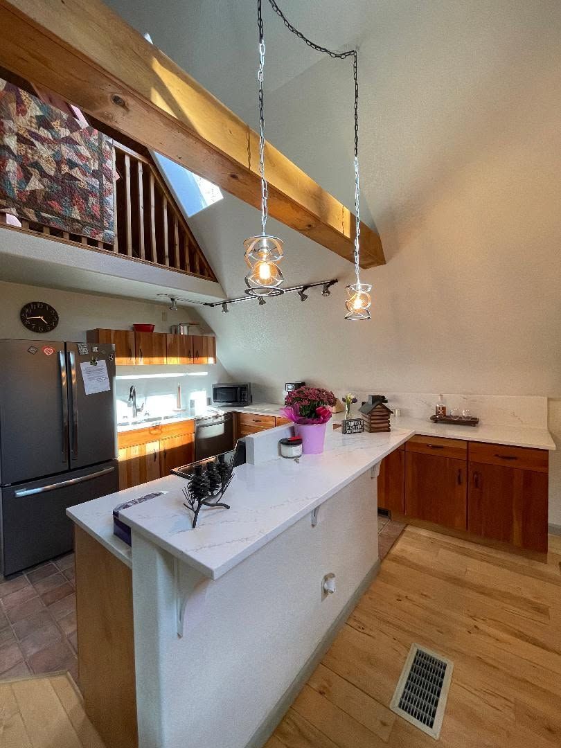 Modern kitchen with white island, wood cabinets, black fridge, and pendant lights under a sloped ceiling