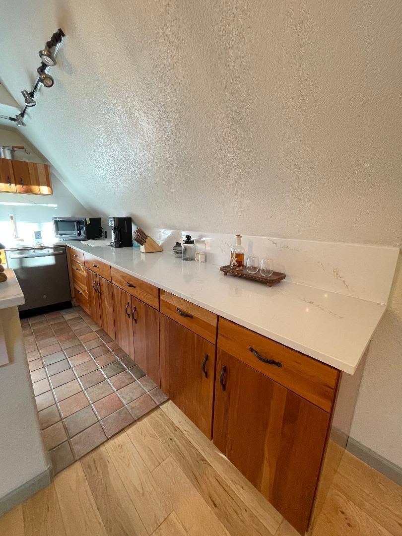 Kitchen with wooden cabinets, white countertops, tiled floor, and sloped ceiling in a narrow room
