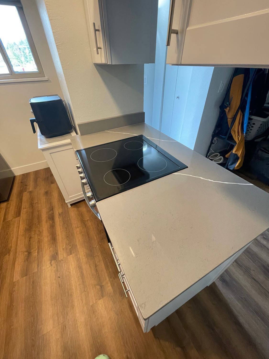Modern kitchen with gray cabinets, wood floor, and a black glass cooktop near a window