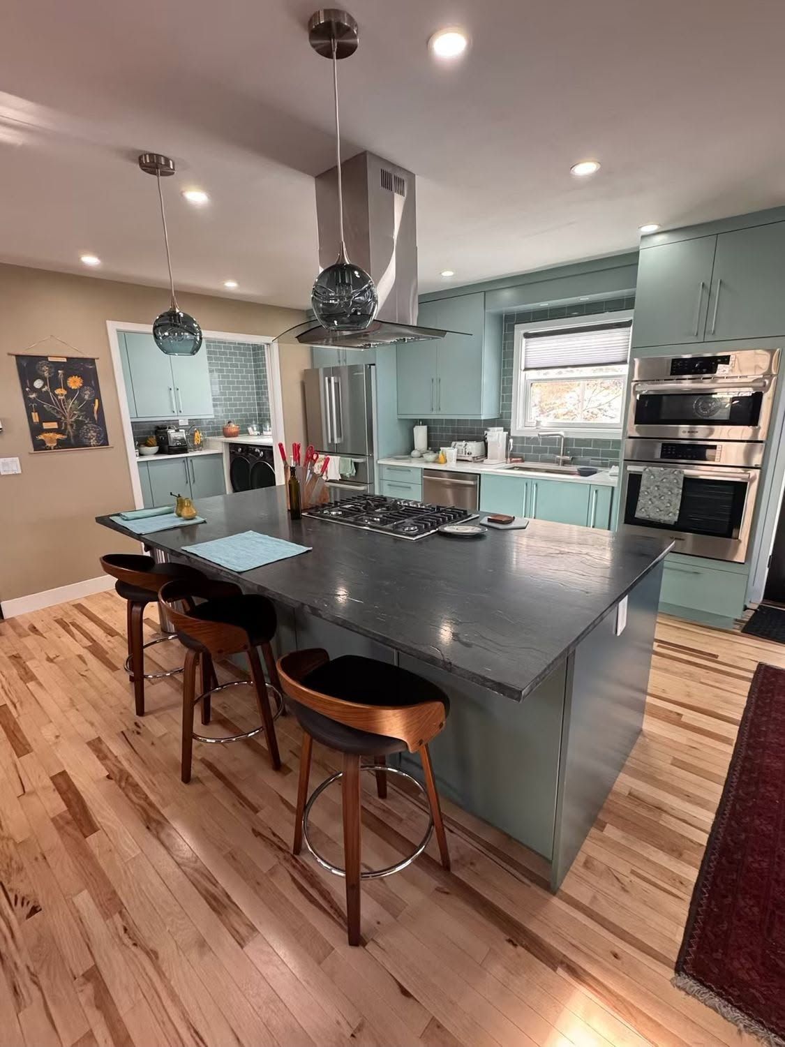 Modern kitchen with a large dark island, bar stools, stainless appliances, and hardwood floors