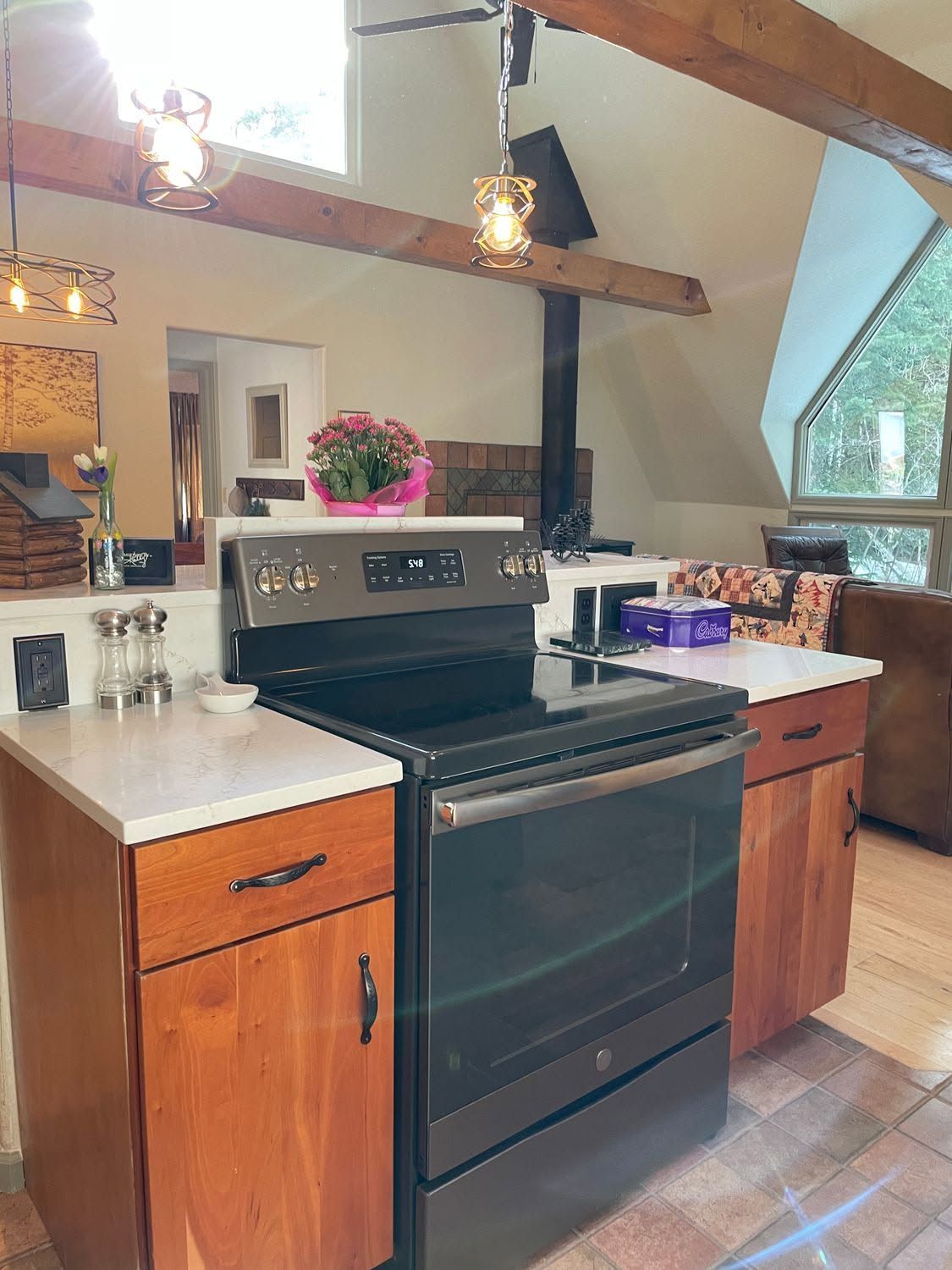 Kitchen with black stove, wood cabinets, white countertops, and hanging pendant lights beneath a vaulted ceiling