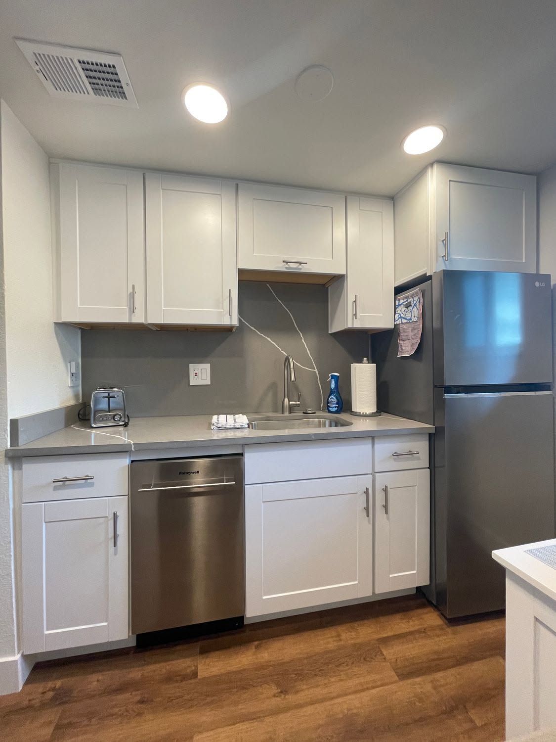 Modern kitchen with white cabinets, stainless steel appliances, gray countertop, and wood floor