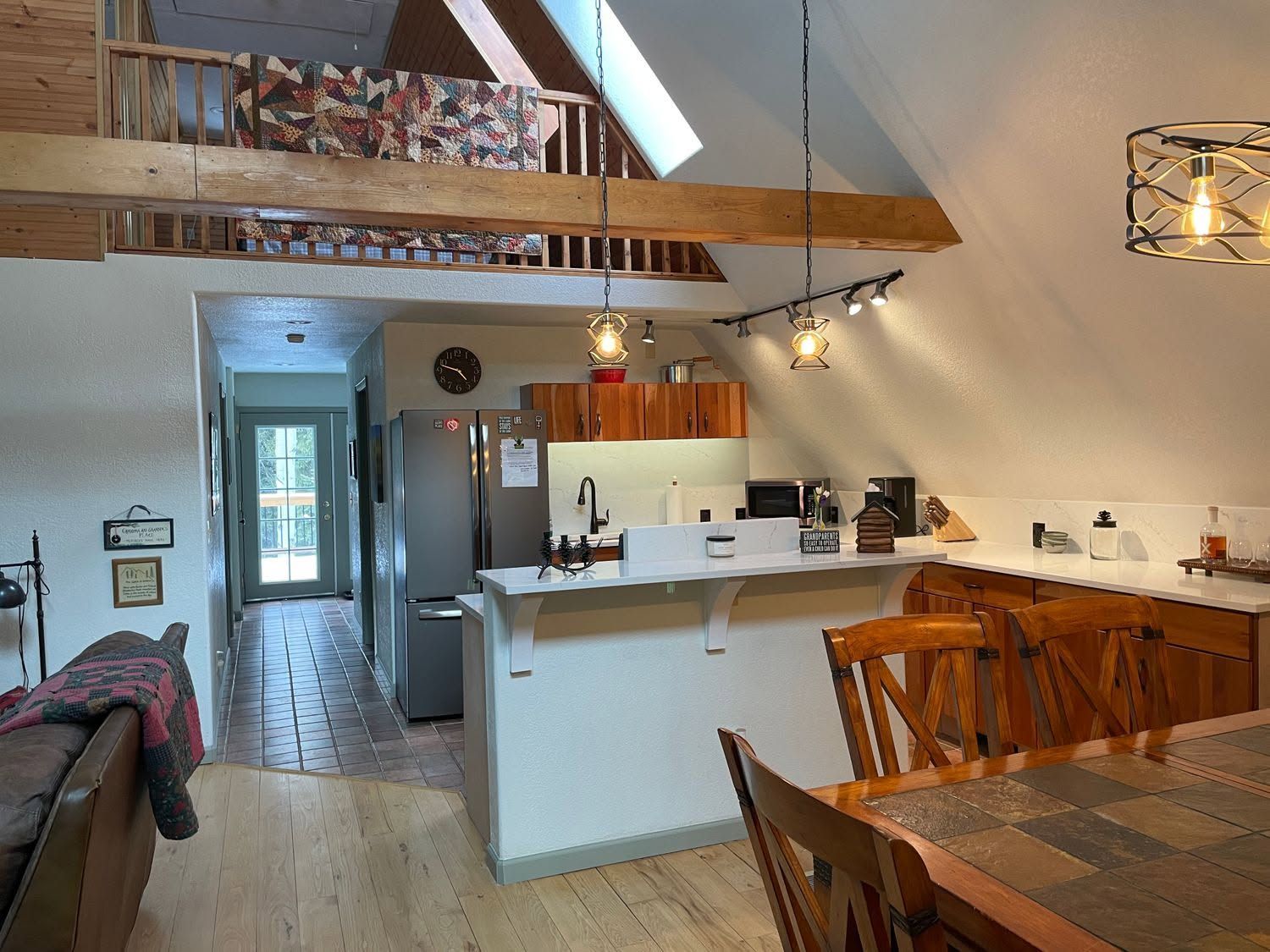 Open-plan kitchen and dining area with wood beams, white cabinets, and a view down a hallway.