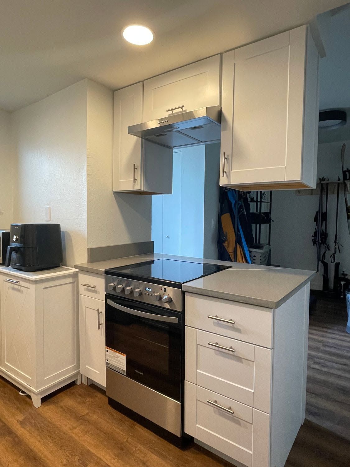 Small white kitchen with a stainless stove, light cabinets, dark countertop, and hardwood floor.