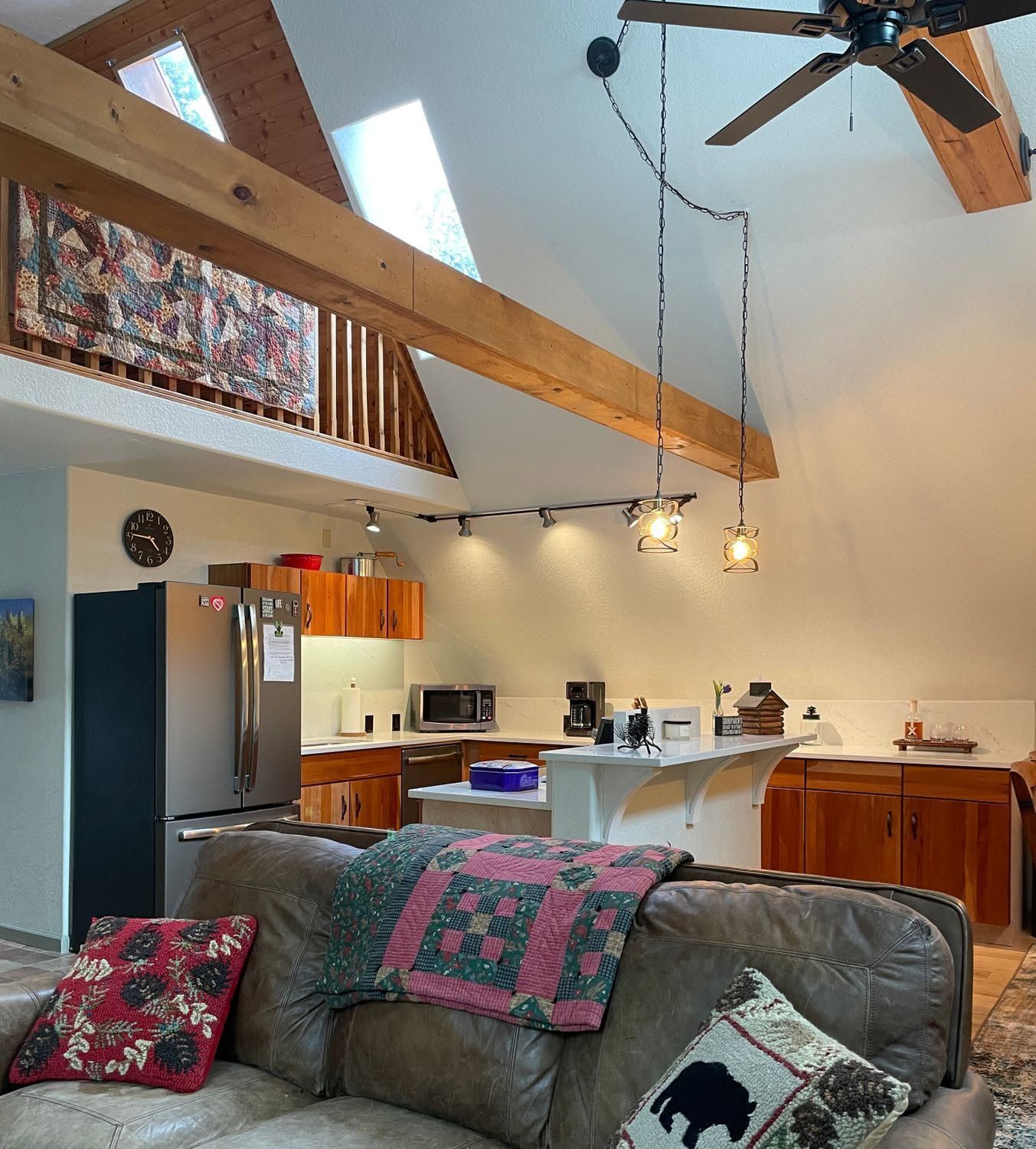 Cozy living room with exposed beams, gray sofa, open kitchen, and hanging pendant lights