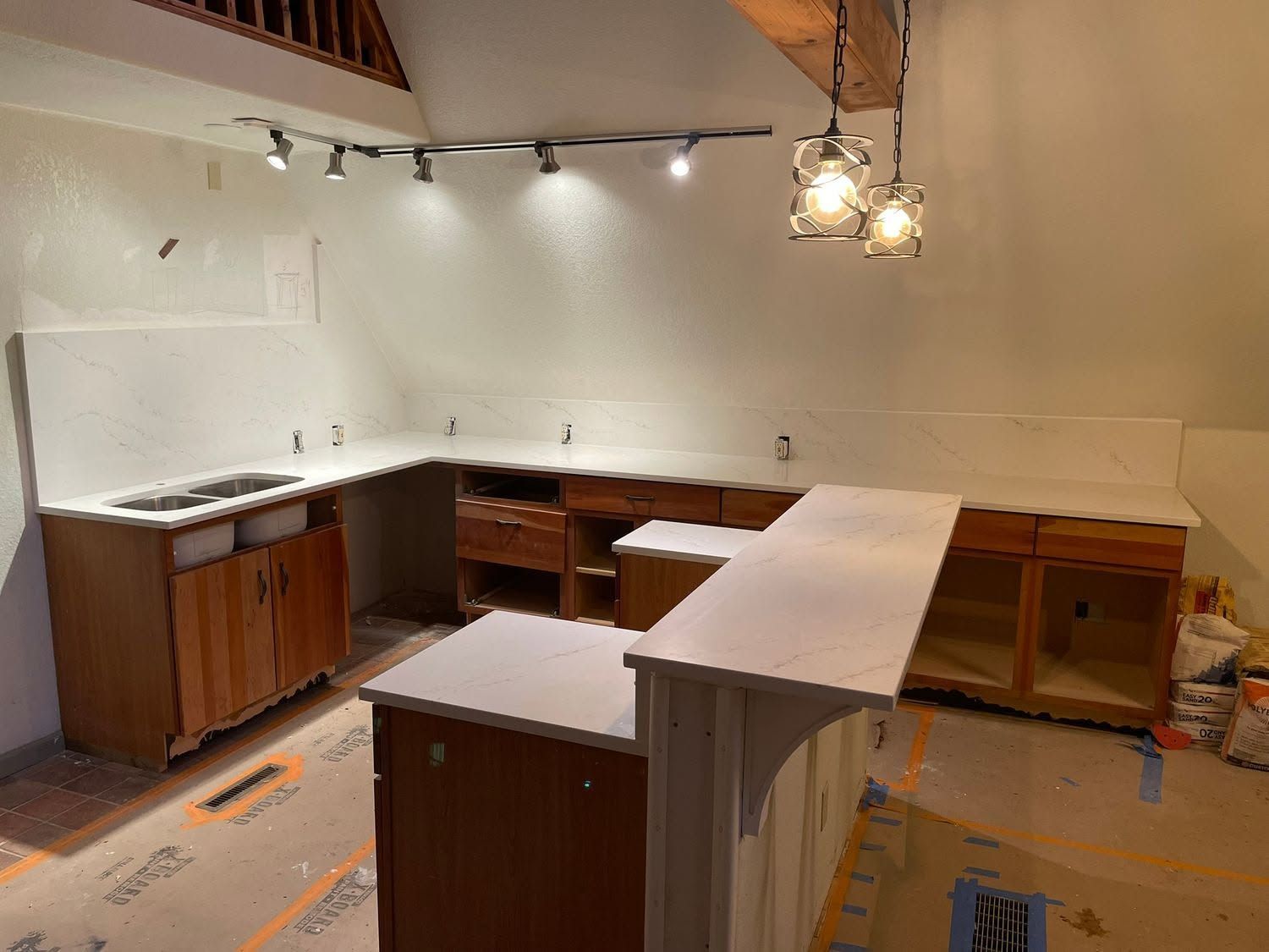 Empty kitchen under renovation with white counters, wood cabinets, and hanging lights