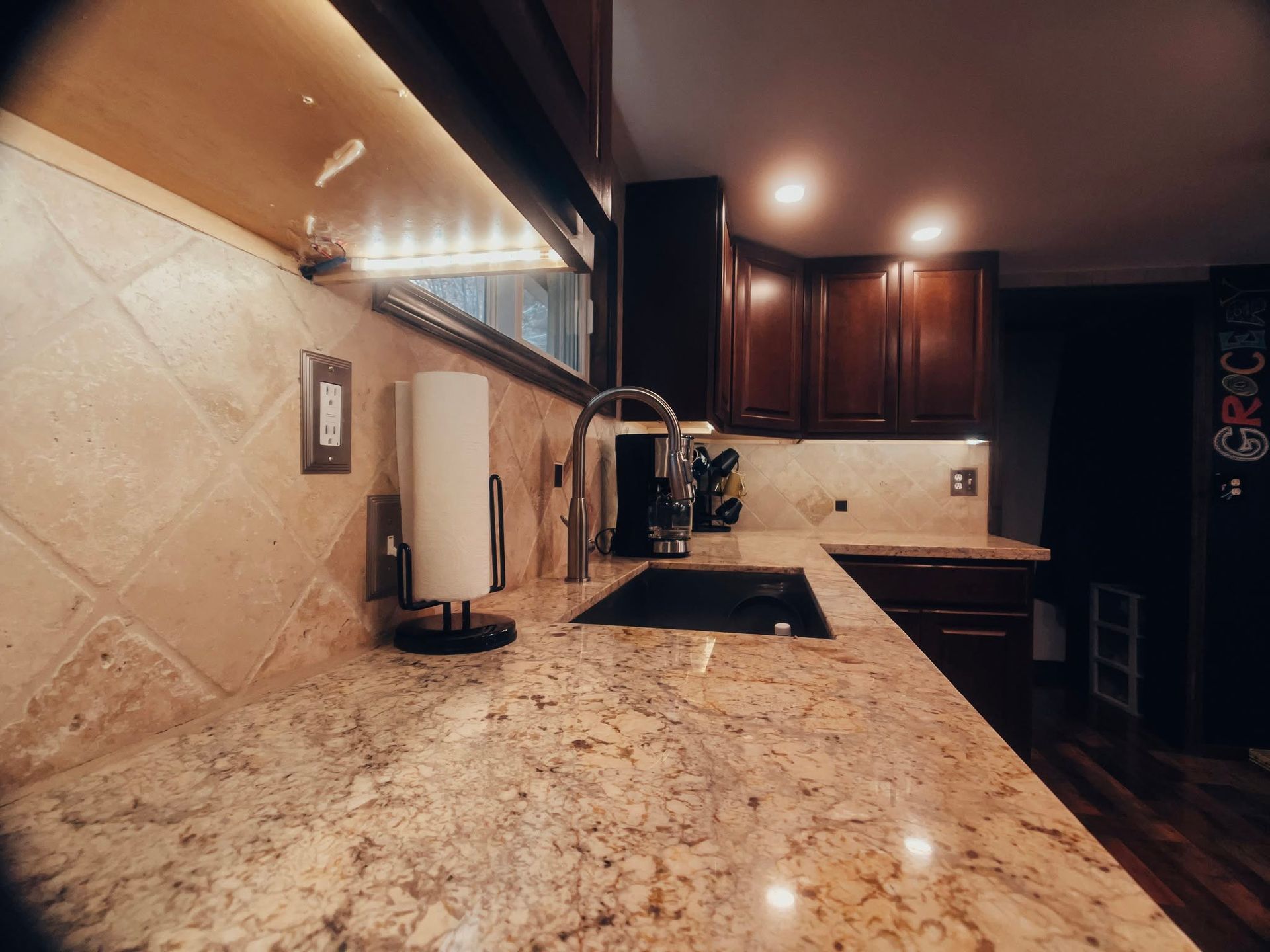 Modern kitchen counter with granite island, dark wood cabinets, and warm recessed lighting