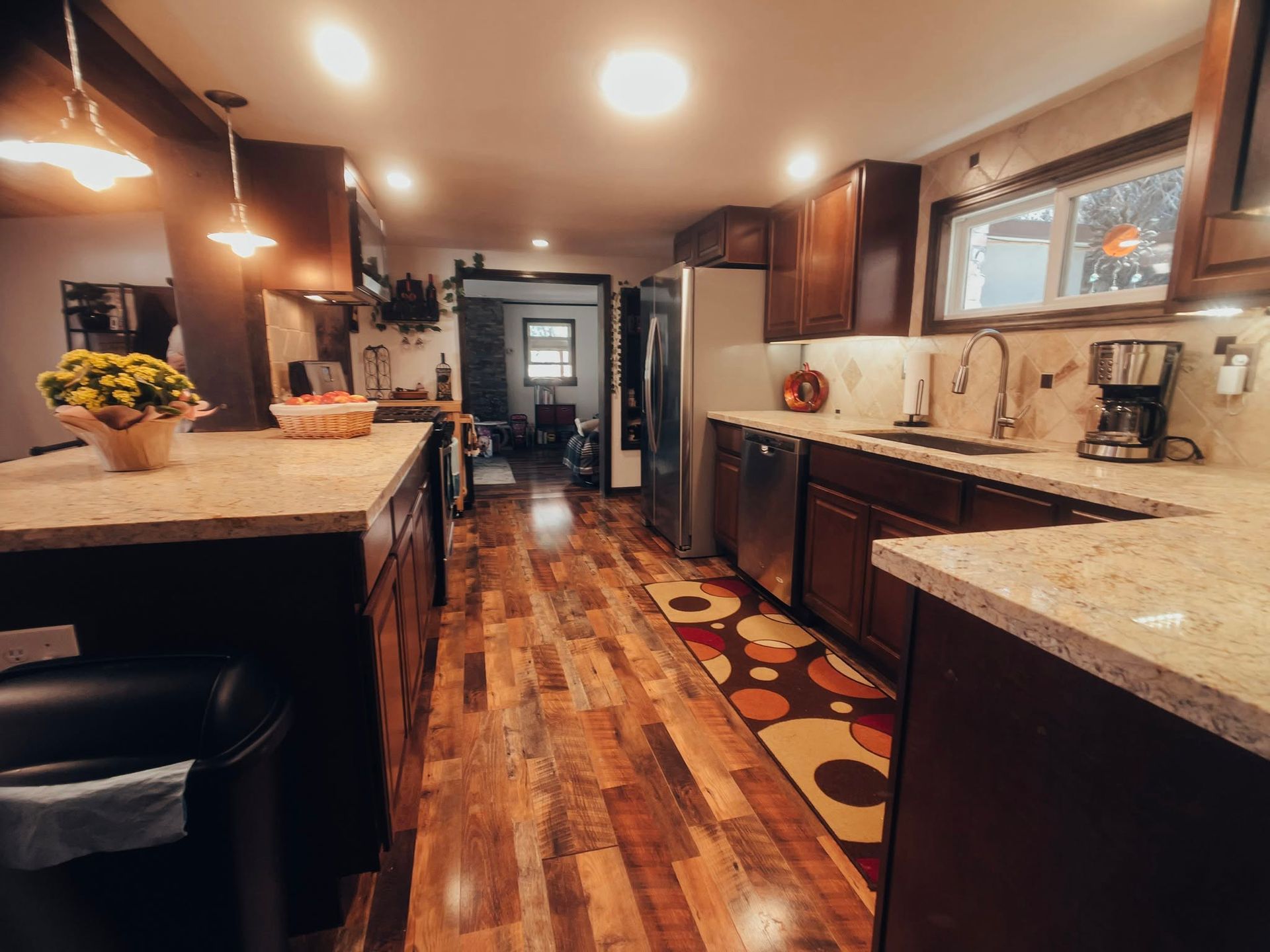 Modern kitchen with dark cabinets, granite counters, wood floor, and patterned runner rug