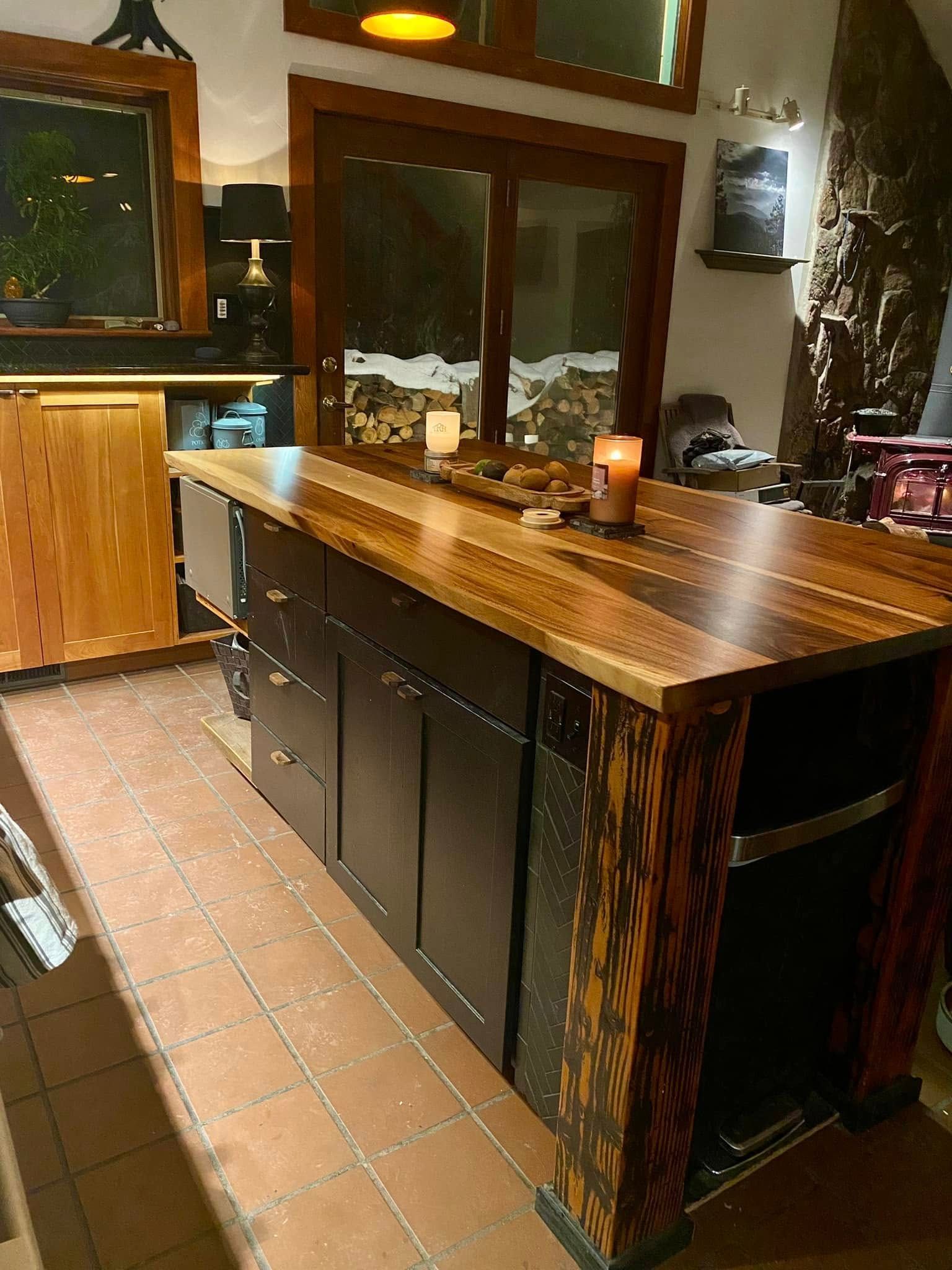 Wooden kitchen island with dark cabinets and tiled floor in a warmly lit room