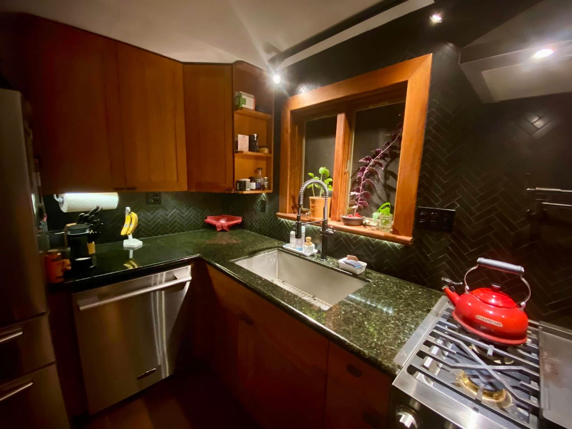 Modern kitchen with dark wood cabinets, black granite counters, stainless sink, and red kettle on the stove