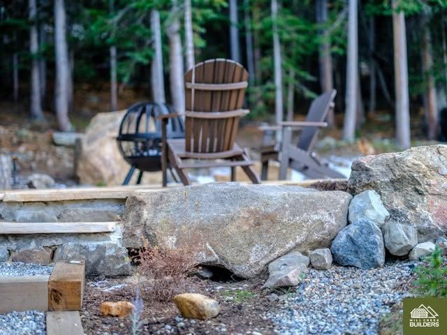Outdoor patio with wooden chairs and a fire pit surrounded by rocks in a wooded setting