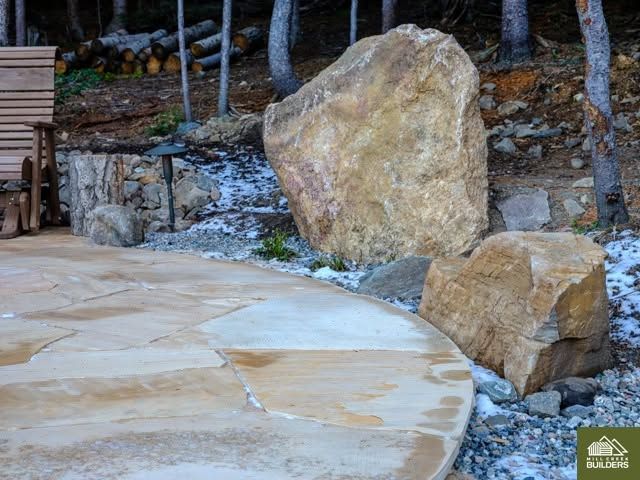 Stone patio with large boulders and trees along a landscaped slope