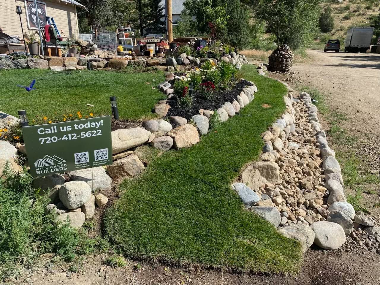 Rock garden landscaping with a green sign, stone border, and grass-covered slope by a road