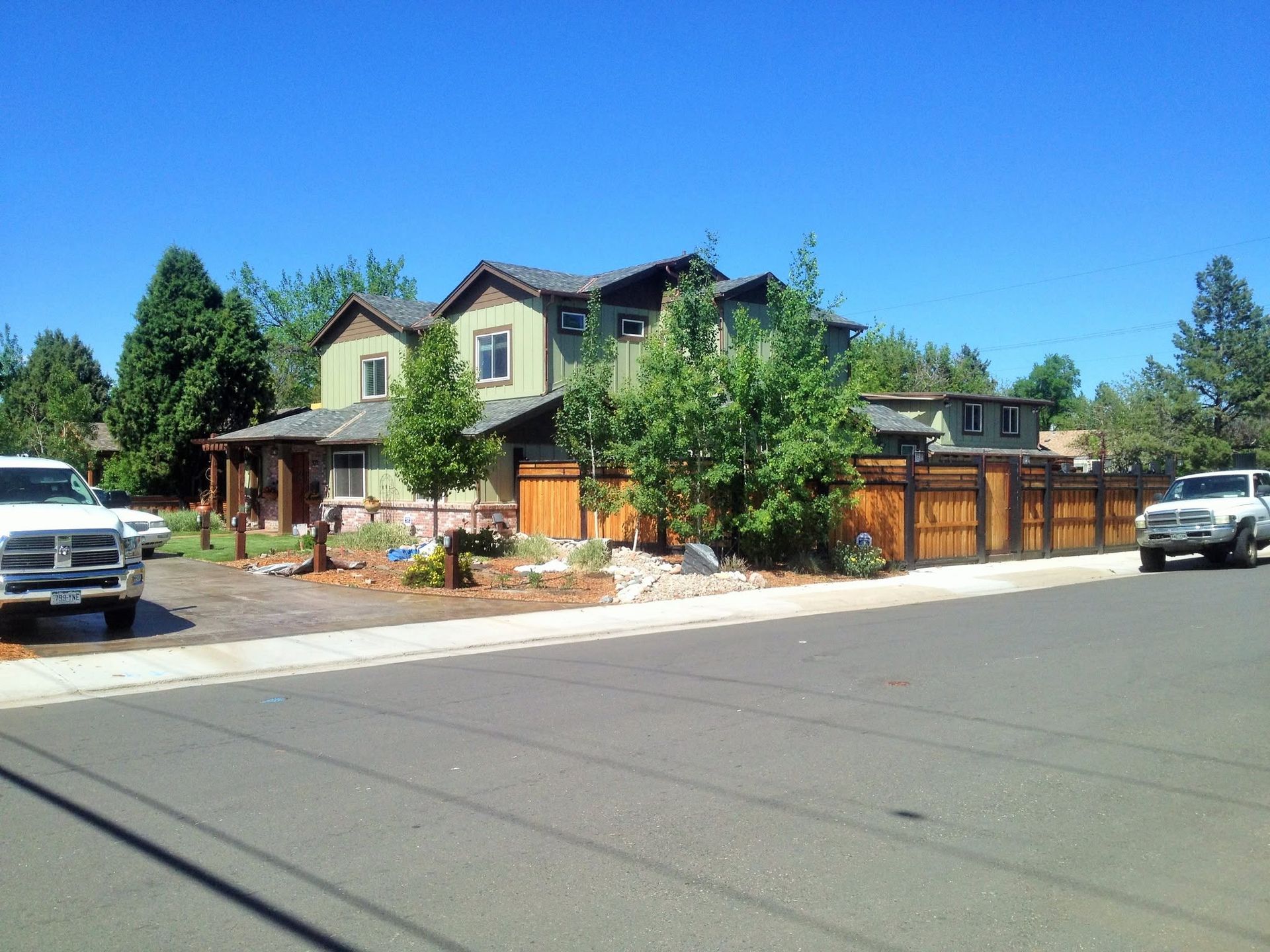 Suburban house with front porch, trees, wooden fence, and parked cars along a quiet street.