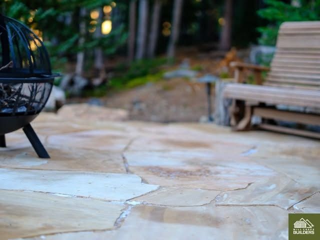 Stone patio with a black hanging chair and a wooden bench in a landscaped garden.
