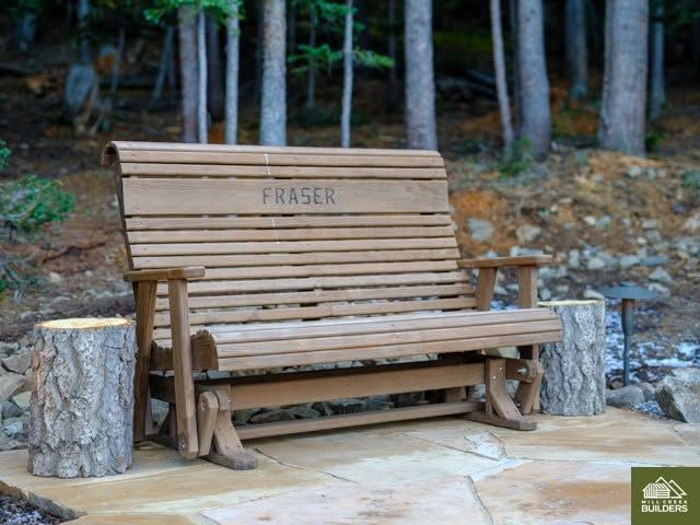 Wooden bench engraved “FRASER” beside tree stumps in a wooded outdoor area