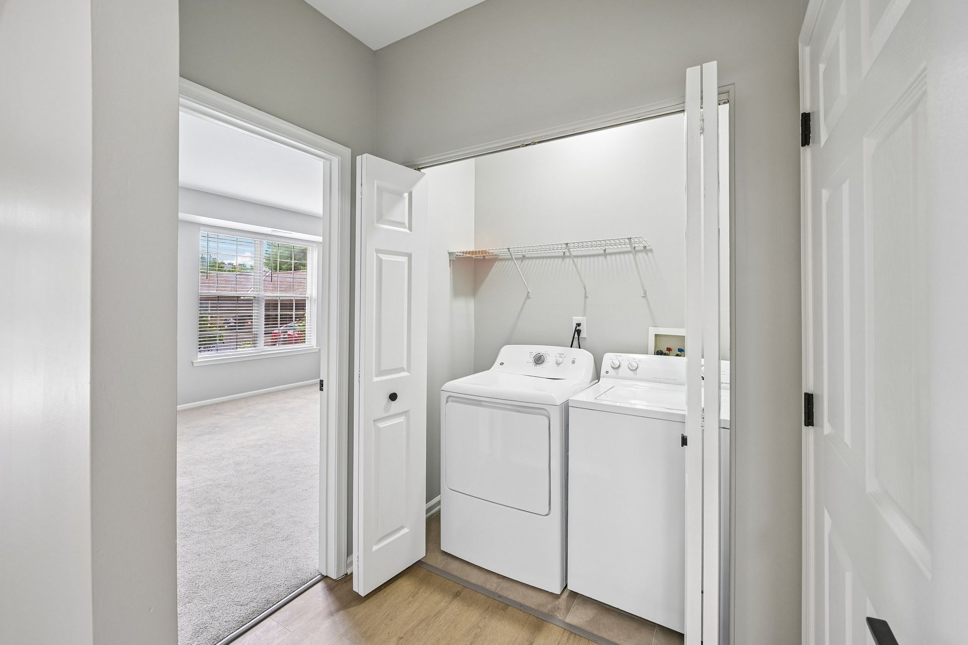 Laundry nook with side by side washer and dryer in a hallway next to a windowed room