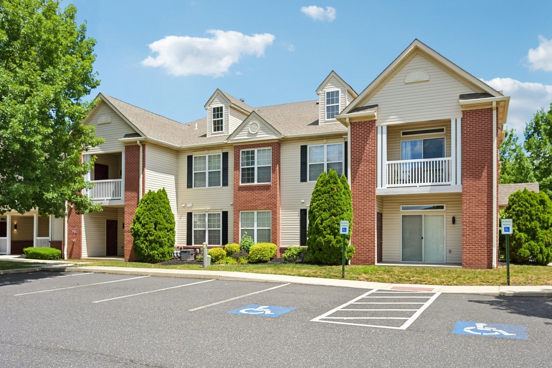 Apartment building with brick and white siding, balconies, and empty accessible parking spaces in front
