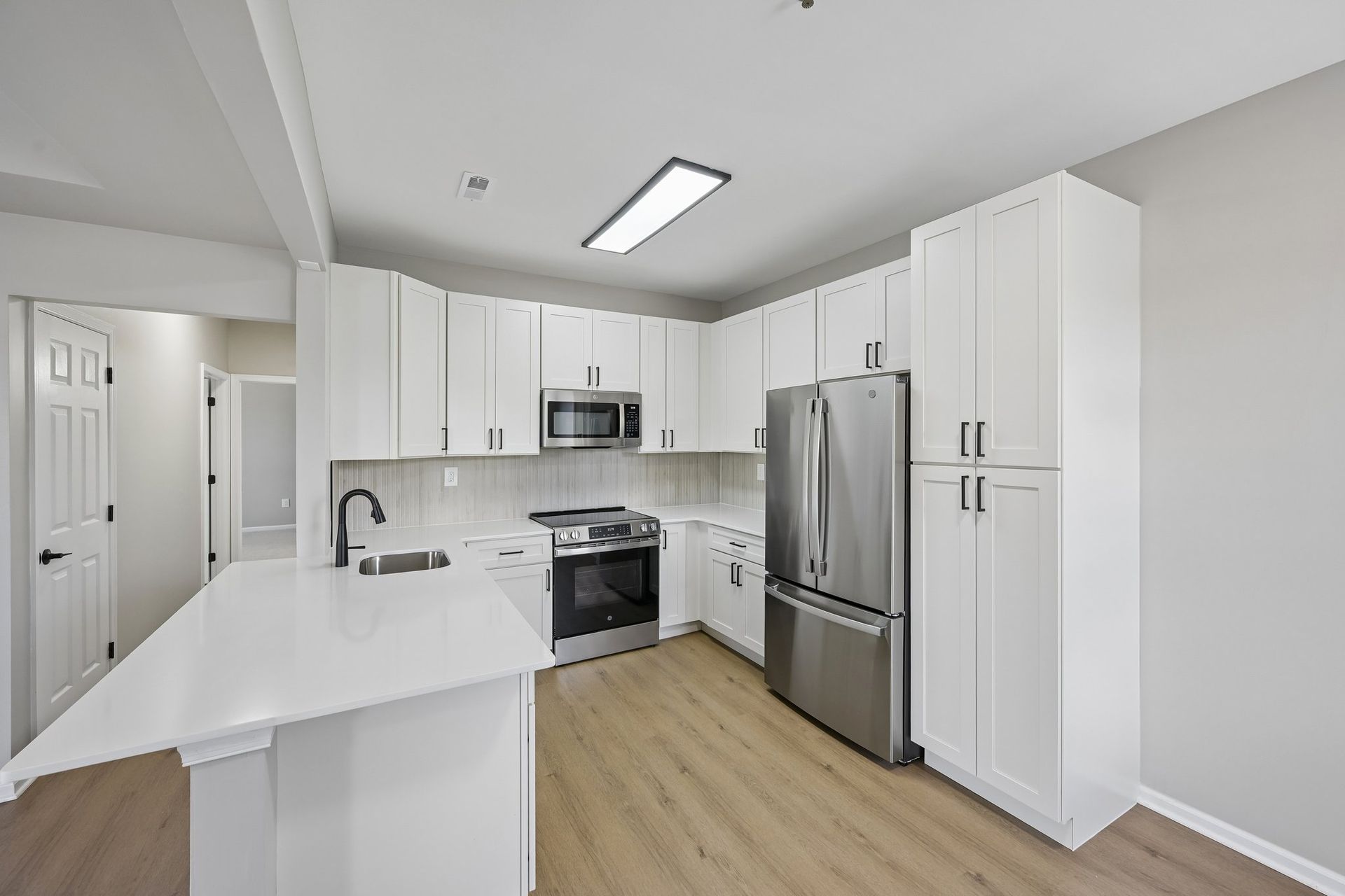 Bright modern white kitchen with stainless steel appliances and wood flooring