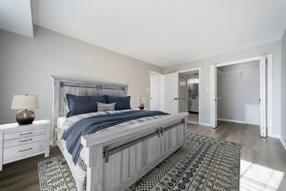 Bedroom with a large bed, neutral gray walls, and an open closet near the bathroom. Visit us at Fox Ridge Apartments and view our modern, garden-style 1 and 2 bedroom apartments in Limerick, PA.