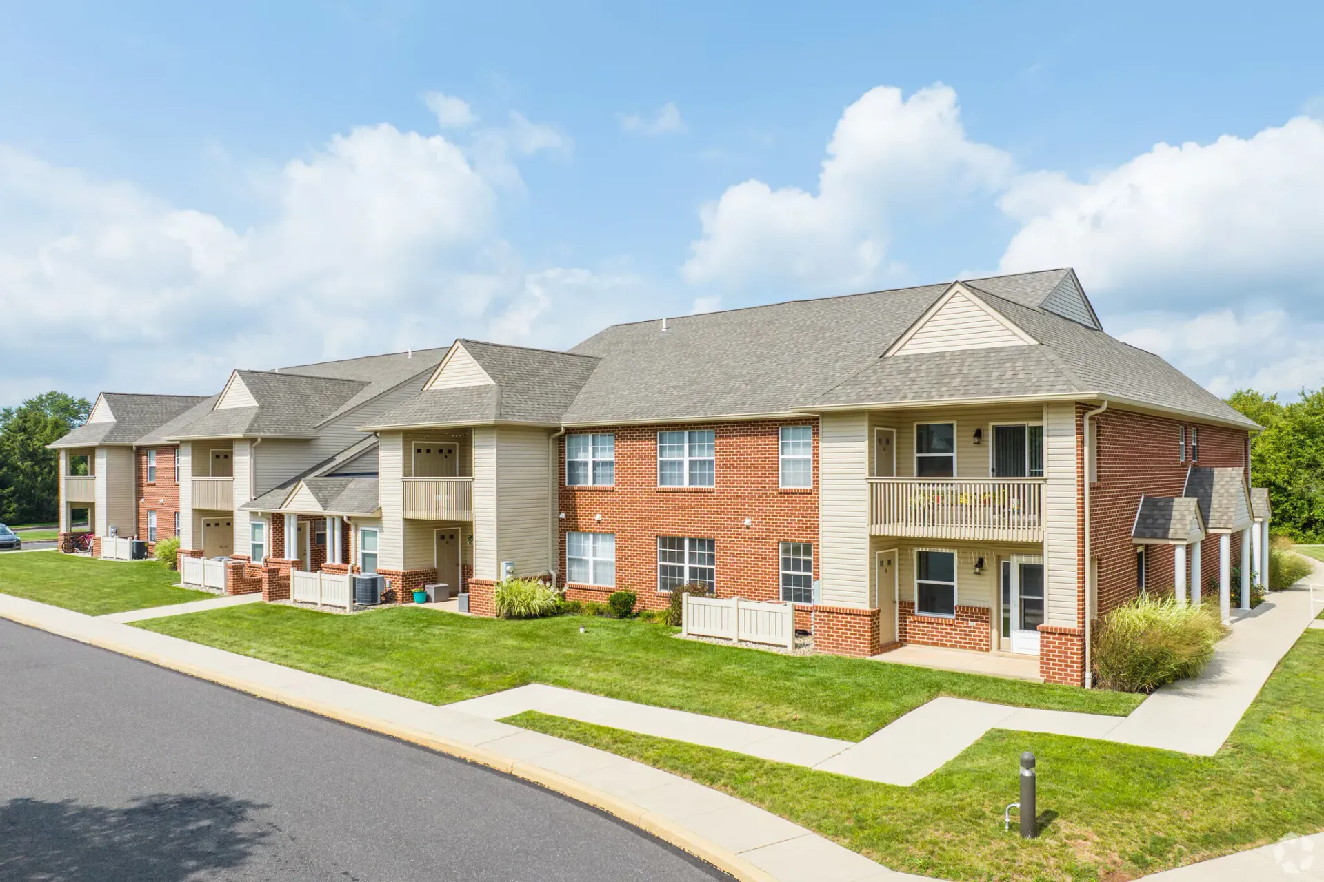 Exterior view of a brick and beige siding apartment building with lawns and sidewalks. Visit us at Fox Ridge Apartments and view our modern, garden-style 1 and 2 bedroom apartments in Limerick and Royersford, PA.