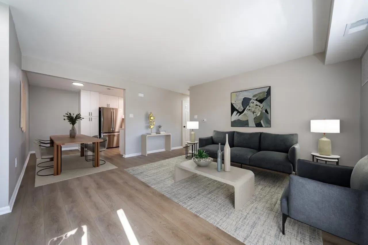 Open-concept living room in a modern apartment with gray sofa, coffee table, and dining area. Visit us at Fox Ridge & Lakeview Park Apartments and view our modern, garden-style 1 and 2 bedroom apartments in Limerick, PA.
