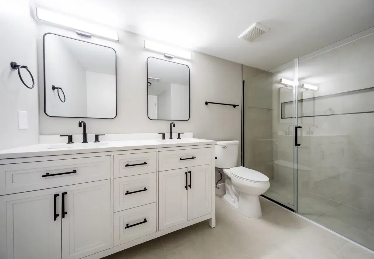 Modern bathroom with a double vanity, two mirrors, and a glass-enclosed shower. Visit us at Fox Ridge & Lakeview Park Apartments and view our modern, garden-style 1 and 2 bedroom apartments in Limerick, PA.