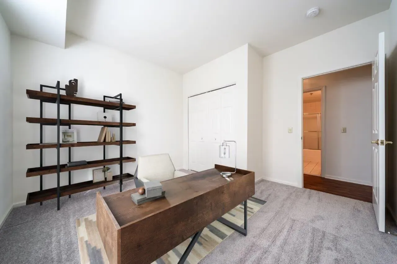 Modern apartment home office with wooden desk, metal shelving, and an open door to a hallway. Visit us at Fox Ridge & Lakeview Park Apartments and view our pet-friendly apartments for rent in Limerick, PA.