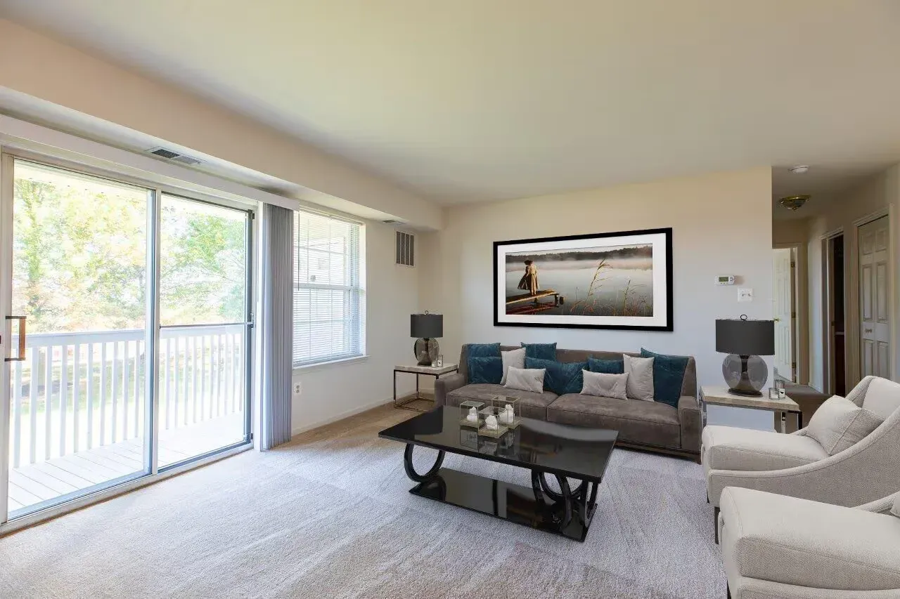 Bright living room in an apartment with a gray sofa, glass coffee table, and sliding balcony doors. Visit us at Fox Ridge & Lakeview Park Apartments and view our modern, garden-style 1 and 2-bedroom apartments in Limerick, PA.