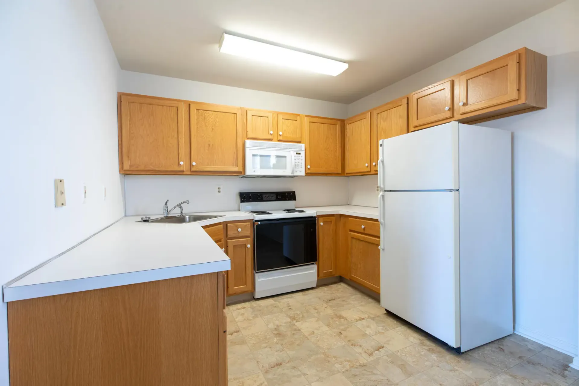 Bright kitchen in an apartment with wood cabinets, white refrigerator, stove, microwave, and sink. Visit us at Fox Ridge & Lakeview Park Apartments and view our pet-friendly apartments for rent in Limerick, PA.
