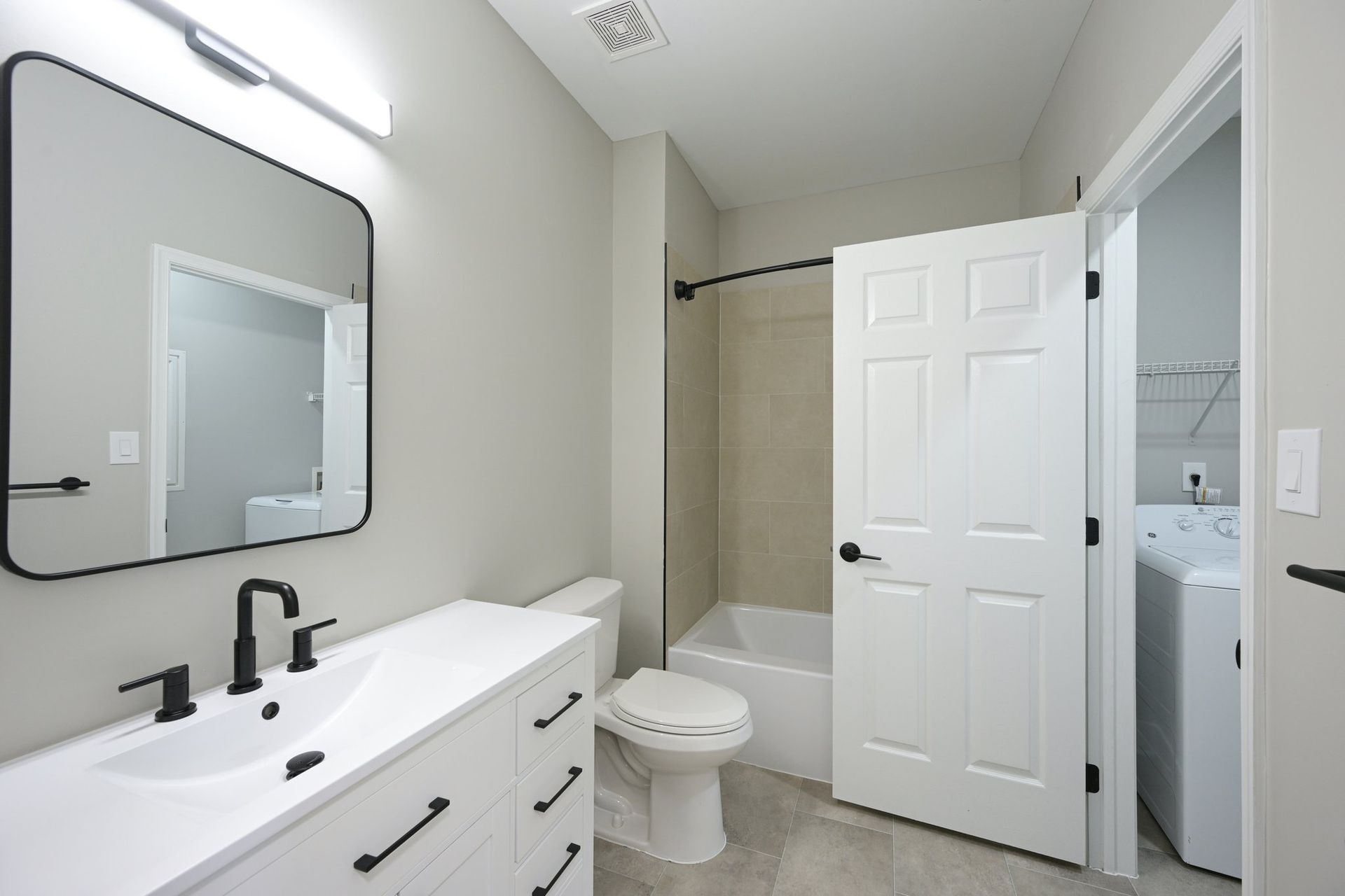 Modern bathroom with white vanity, black fixtures, mirror, toilet, and in-unit laundry