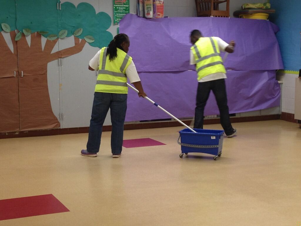 A man and a woman cleaning a floor with a mop