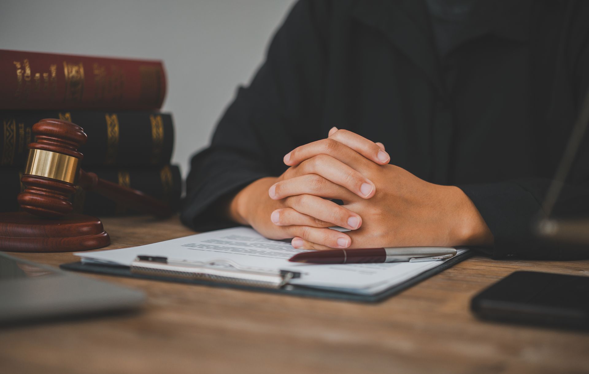 Hands clasped over legal documents beside a gavel on a courtroom desk