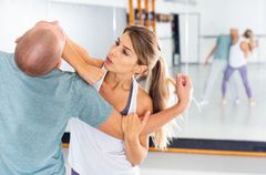 A man and a woman are practicing self defense in a gym.
