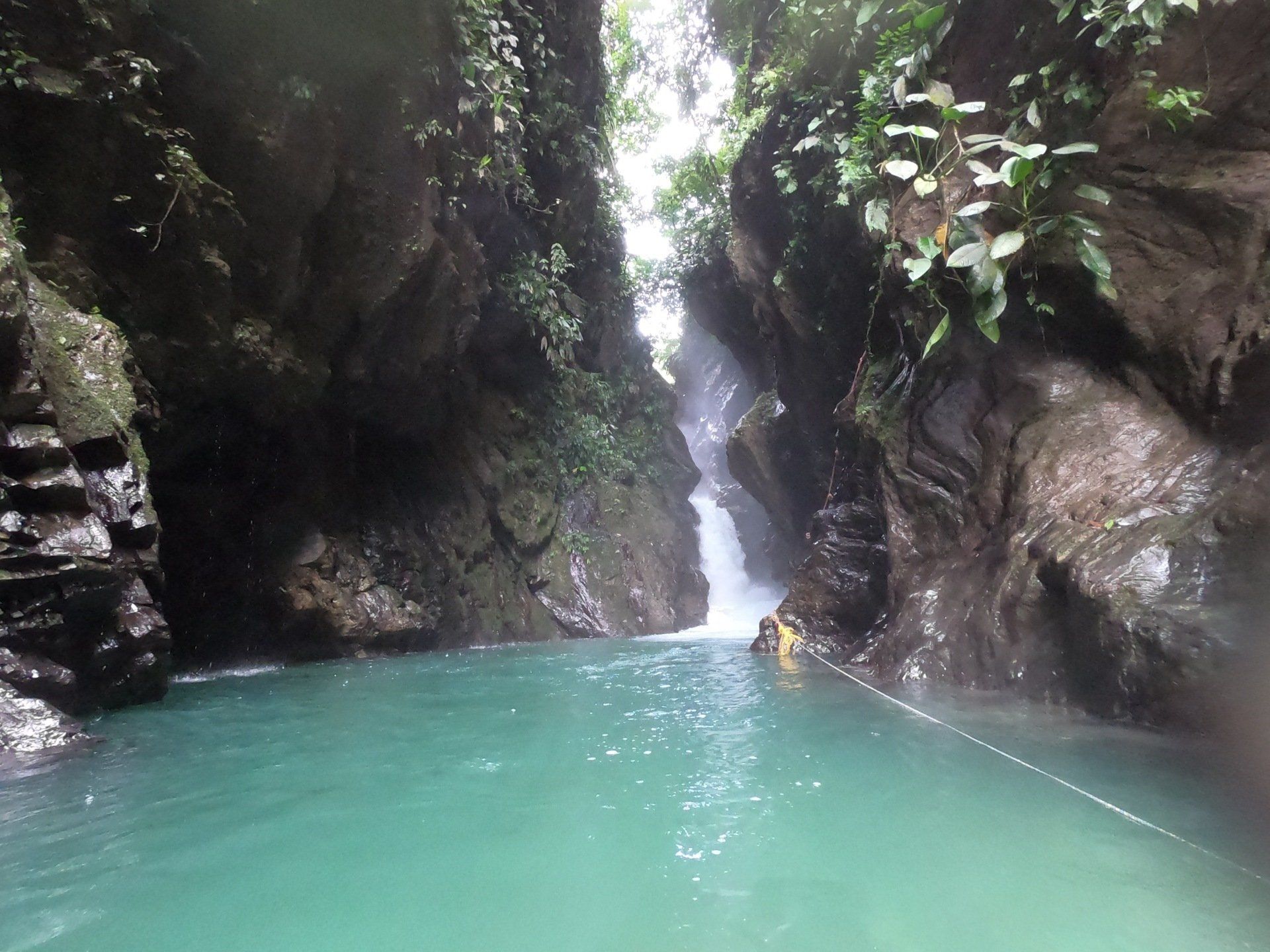 Cascada tropical que cae en una poza de color turquesa entre oscuros acantilados rocosos y exuberante vegetación.
