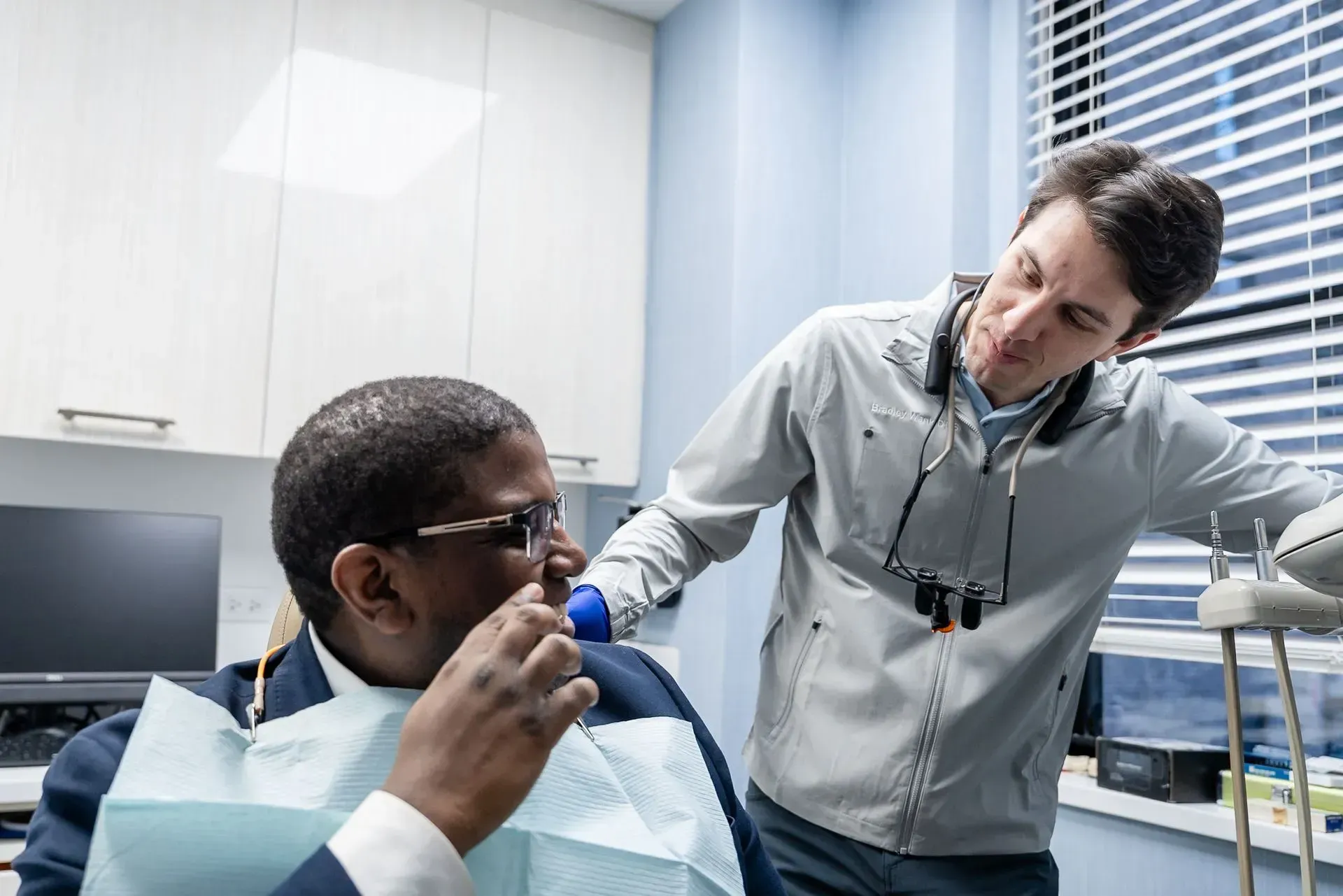 Dentist examines a patient in a dental clinic while speaking with him.